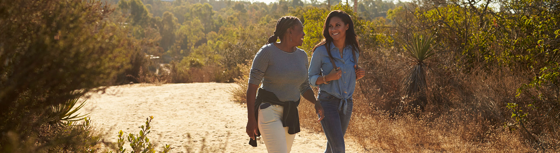 two women walking and smiling on hiking trail.